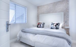 Biała, nowoczesna sypialnia z tapetą imitującą cegłę za łóżkiem. 